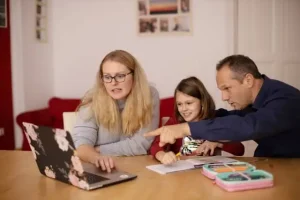 Padres y niña usando una tablet juntos en casa, aprendiendo sobre tecnología familiar